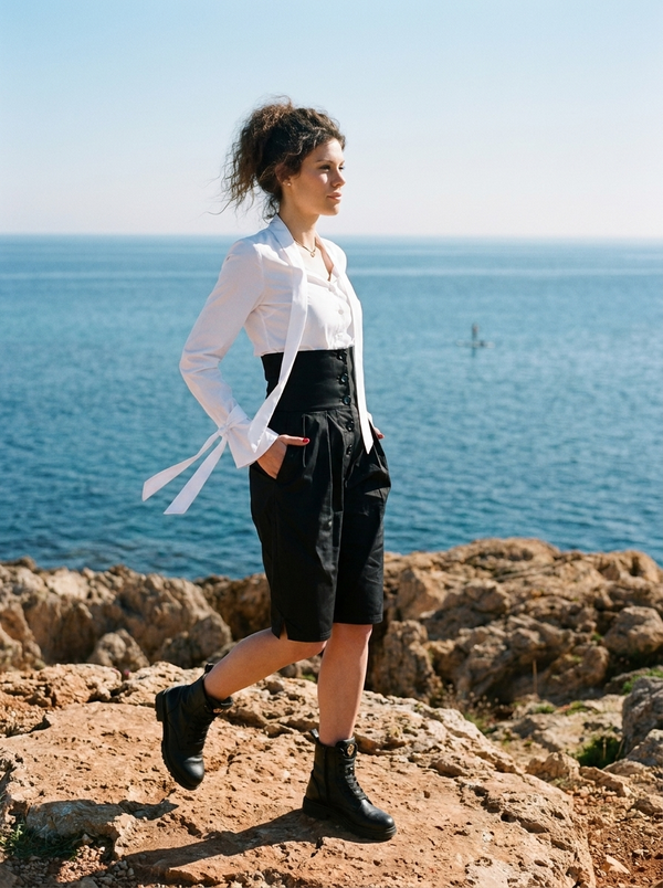 Black high-waist button-front midi shorts on Mediterranean seaside rocks — Souls In Clothes